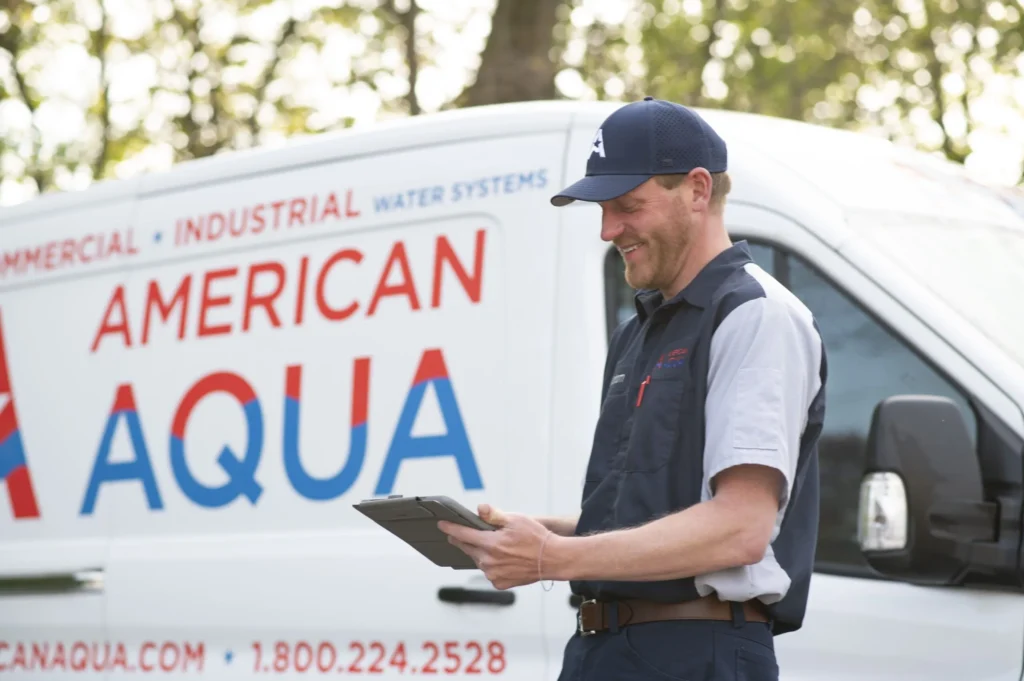 a Male American Aqua employee smiling while using a tablet in front of an American Aqua branded white van.