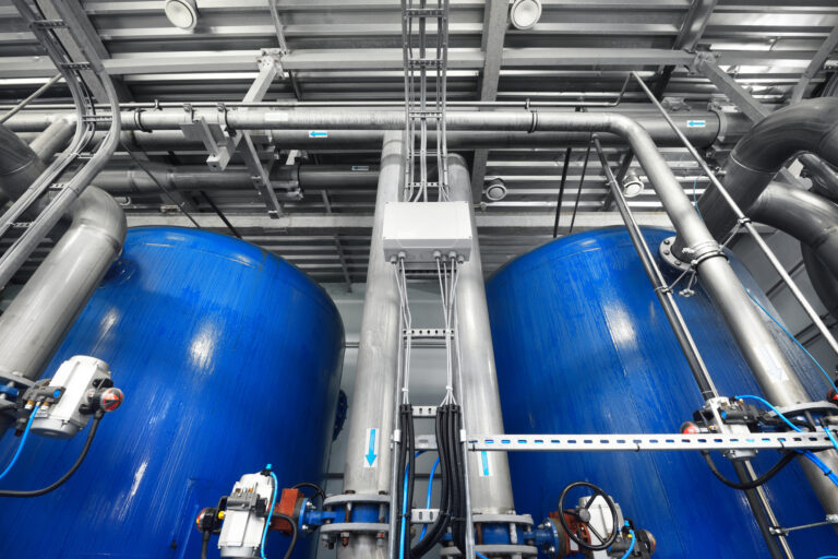 Large industrial water treatment and boiler room. Shiny steel metal pipes and blue pumps and valves.