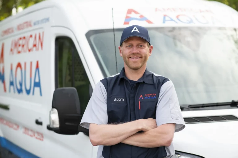 A male American Aqua employee wearing an American Aqua branded shirt and navy blue hat. He is standing in front of an American Aqua branded white van.